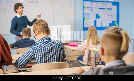 Fürsorglicher Lehrer erklärt Lektion zu einem Klassenzimmer voller heller vielfältiger Kinder. In der Grundschule mit Gruppe von Smart Multiethnic Learning Science Stockfoto