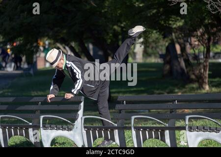 Ein älterer Mann in einem Hut streckt sich, während er in einem Park in Queens, New York City, festhält. Stockfoto