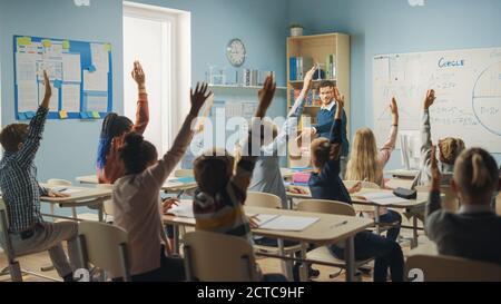 Fürsorglicher Lehrer erklärt Lektion zu einem Klassenzimmer voller heller vielfältiger Kinder. In der Grundschule mit Gruppe von intelligenten multiethnischen Kinder lernen Stockfoto