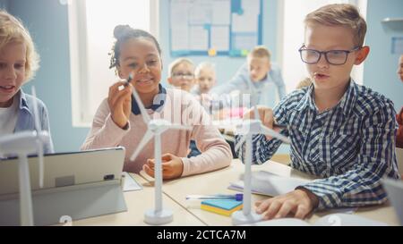 In der Grundschule: Klasse der brillanten jungen Kinder arbeiten als Team mit Tablet-Computern zu programmieren Windturbinen. Klassenraum mit Kindern Stockfoto