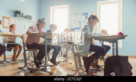 Aufnahme eines Klassenzimmers voller Kinder. In der Grundschule Gruppe der Smart multiethnischen Kinder Schreiben in Übung Notebooks und Lernen. Niedrig Stockfoto