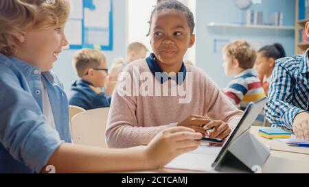 In der Grundschule: Mädchen und ein Junge arbeiten als Team mit Tablet-Computern, Programmiersprache lernen, Internet-Sicherheit und Robotik-Design Stockfoto