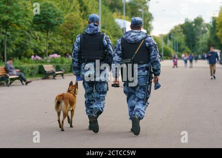 Polizeistreife im öffentlichen Stadtpark von Moskau. Zwei Offiziere mit Hund. Sicherheits- und Sicherheitskonzepte. Rückansicht/Rückansicht. Coronavirus-Pandemiezeit. Stockfoto