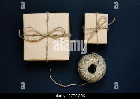Handgefertigte Geschenkbox in Bastelpapier mit Seil und Schleife auf schwarzem Hintergrund verpackt. Draufsicht, flach liegend Stockfoto