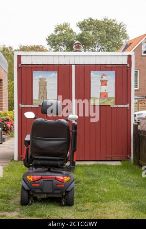 Elektrischer Rollstuhl auf Rasen vor Garage, Borkum Island, Friesland, Niedersachsen, Deutschland, Europa geparkt. Stockfoto