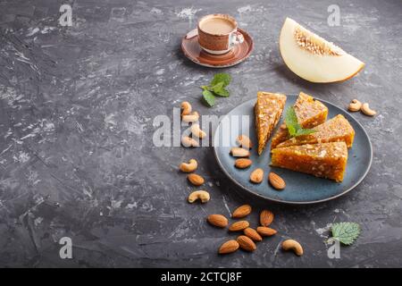 Traditionelle türkische Süßwaren-Cezerye aus karamellisierter Melone, gerösteten Walnüssen, Haselnüssen, Cashew, Pistazien in blauer Keramikplatte und einer Tasse Kaffee Stockfoto