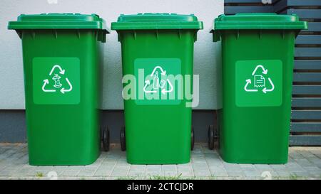 Grün gefärbte Plastikmüllbehälter, mit verschiedenen Recycling-Logos auf der Vorderseite, in Reihe gegen braune Holzwand gestapelt. Konzept der Abfallsortierung für Lebensmittel Stockfoto