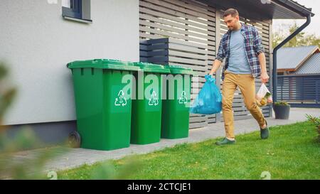 Kaukasischer Mann ist zu Fuß vor seinem Haus, um zwei Plastiktüten des Mülls zu nehmen. Eine Mülltüte wird als biologischer Lebensmittelabfall, andere sortiert Stockfoto