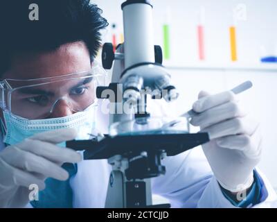 Asiatischer Wissenschaftler arbeitet ernsthaft Chemie Experiment mit einem Mikroskop im Labor, das Farbtonbild. Stockfoto