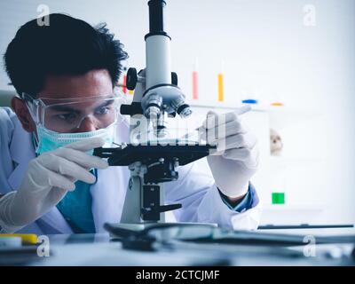Asiatischer Wissenschaftler arbeitet ernsthaft Chemie Experiment mit einem Mikroskop im Labor, das Farbtonbild. Stockfoto