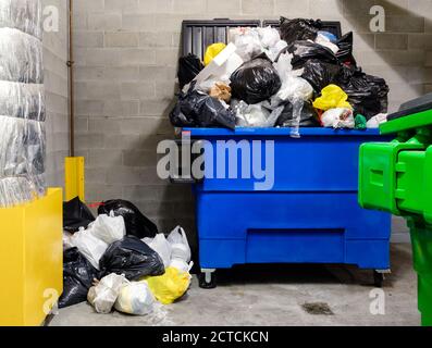 Überlastete Haushaltsmüllbehälter in Müllraum des Wohngebäudes. Das Entsorgungsunternehmen hat aufgrund von Schneesturm die Abholung verpasst. Stockfoto