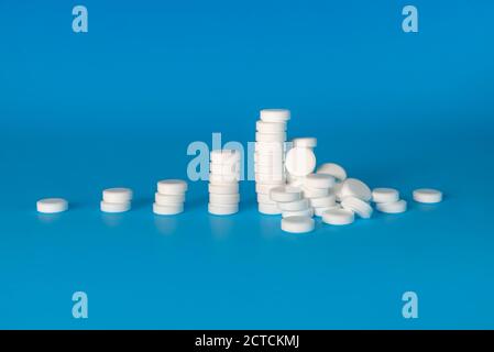 Drogenkonsum Eskalation, Drogenmissbrauch oder Suchtkonzept. Weiße Pillenstapel wachsen von links nach rechts und enden mit einem Stapel von Pillen umgefallen. Stockfoto