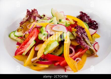 Gemüsesalat mit Gurken, Tomaten, Rettich, Rettich, Paprika, Zwiebeln und Salat. Nahaufnahme auf einem weißen Teller. Stockfoto