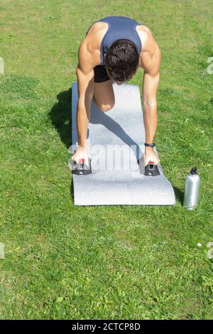 Ein Teenager-Junge in Sportbekleidung macht Liegestütze mit Trainingsgriffen Im Garten zusammen mit einer Flasche Wasser auf Ein sonniger Tag Stockfoto