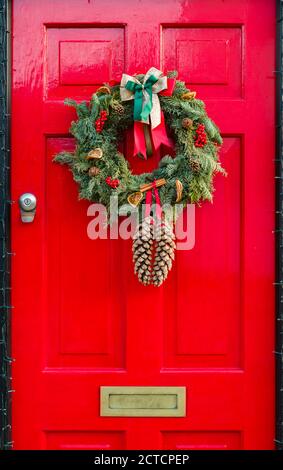 Detail der hölzernen Vordertür zu einem britischen Haus gemalt Ein festliches leuchtendes Rot mit Weihnachtskranz Stockfoto