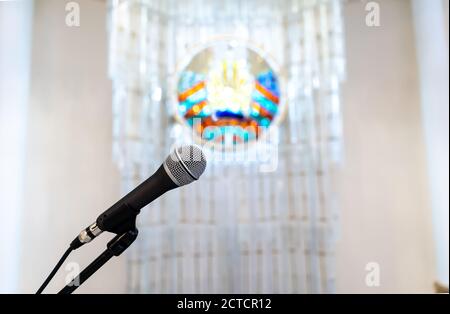 Tribüne mit Mikrofon auf dem Hintergrund des verschwommenen weißrussischen Wappens. Stockfoto