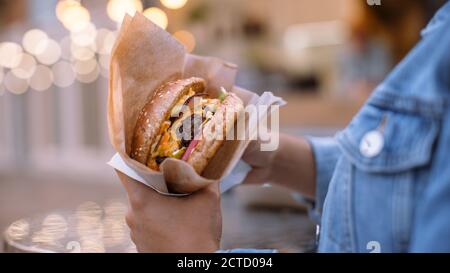 Nahaufnahme von einem leckeren Burger. Junge Person hält Burger mit Flaming Hot Grounded Beef Patty mit geschmolzenem Käse zu einem Burger Bun mit Salat Stockfoto