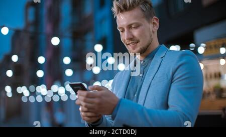 Handsome Young Concentrate man benutzt ein Smartphone, während man abends im Freien steht. Er ist im Internet oder in sozialen Medien surfen, Posting A Stockfoto