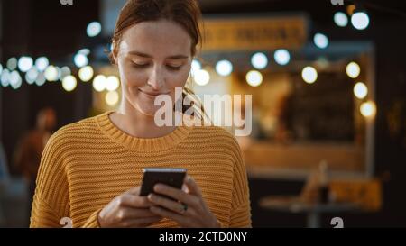 Schöne Brünette junge Frau ist mit einem Smartphone, während im Freien am Abend stehen. Sie ist im Internet oder in sozialen Medien, Posting a Stockfoto
