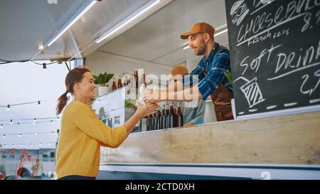 Food Truck Employee überreicht einen frisch zubereiteten Gourmet Burger an eine glückliche junge Frau. Street Food Truck verkauft Burger in einem modernen Hip Nachbarschaft. Stockfoto