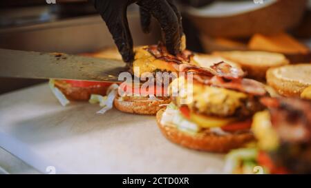 Tasty Close Up Shot von einem Koch Vorbereitung Burger. Food Chef fügt Souce auf Brötchen mit Sesamsamen hinzu. Frische Gourmet Burger mit Rindfleisch Patty Stockfoto