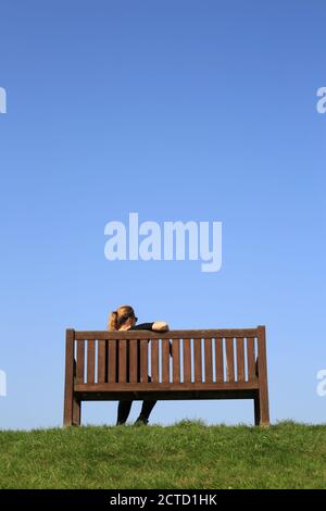 Frau, die allein auf einer Holzbank sitzt. Stockfoto