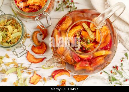 Vitamin Kräutertee. Köstliches und gesundes warmes Herbstgetränk aus getrockneten Äpfeln, Linden, Erdbeeren in einer Glas-Teekanne auf einem weißen Tisch. Sele Stockfoto