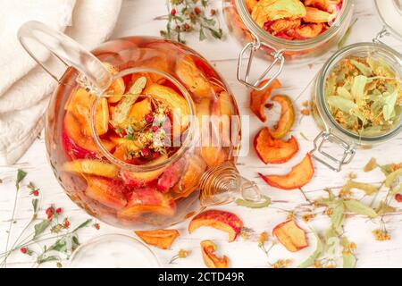 Vitamin Kräutertee. Köstliches und gesundes warmes Herbstgetränk aus getrockneten Äpfeln, Linden, Erdbeeren in einer Glas-Teekanne auf einem weißen Tisch. Sele Stockfoto
