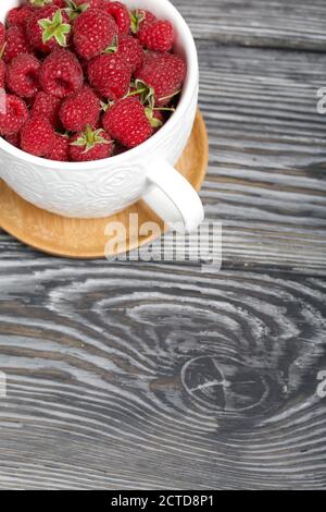 Himbeeren in einem großen weißen Becher. Auf Holzbrettern mit einer schönen Textur. Stockfoto