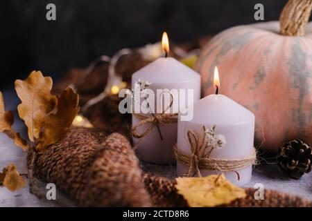 Dunkle Herbstkomposition. Kürbisse mit brennenden Kerzen, Strickpullover, Girlande und getrockneten Blättern. Herbst, Herbst, halloween Konzept Stockfoto