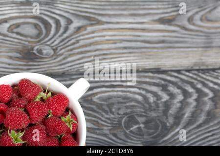 Himbeeren in einem großen weißen Becher. Auf Holzbrettern mit einer schönen Textur. Stockfoto