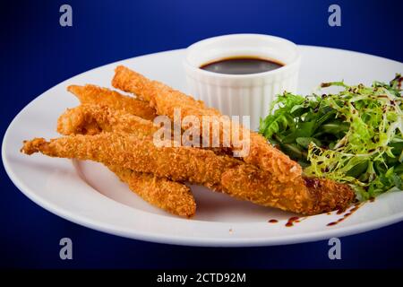 Panierte Hähnchenstreifen mit Sauce und Salatblättern. Nahaufnahme auf einem weißen Teller. Stockfoto