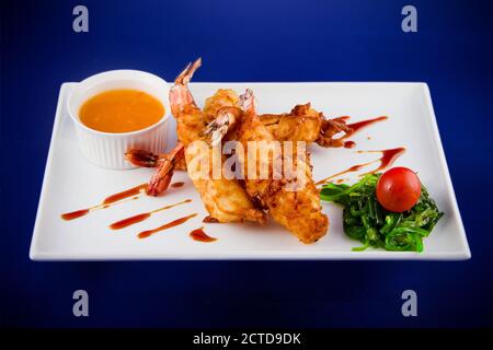 Gebratene Tigergarnelen im Teig serviert mit süßer und saurer Sauce, Nori-Algen und Kirschtomaten auf einem rechteckigen Teller. Stockfoto