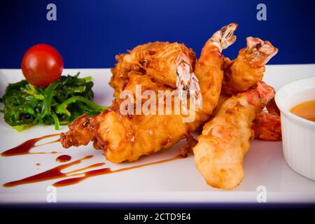 Gebratene Tigergarnelen im Teig serviert mit süßer und saurer Sauce, Nori-Algen und Kirschtomaten auf einem rechteckigen Teller. Stockfoto