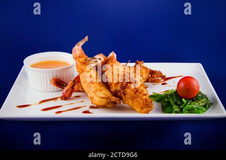 Gebratene Tigergarnelen im Teig serviert mit süßer und saurer Sauce, Nori-Algen und Kirschtomaten auf einem rechteckigen Teller. Stockfoto