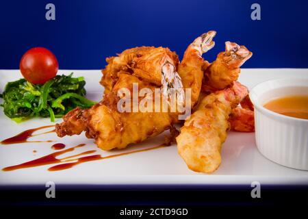 Gebratene Tigergarnelen im Teig serviert mit süßer und saurer Sauce, Nori-Algen und Kirschtomaten auf einem rechteckigen Teller. Stockfoto