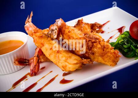 Gebratene Tigergarnelen im Teig serviert mit süßer und saurer Sauce, Nori-Algen und Kirschtomaten auf einem rechteckigen Teller. Stockfoto