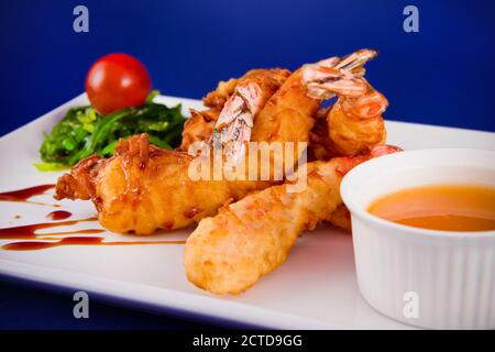 Gebratene Tigergarnelen im Teig serviert mit süßer und saurer Sauce, Nori-Algen und Kirschtomaten auf einem rechteckigen Teller. Stockfoto