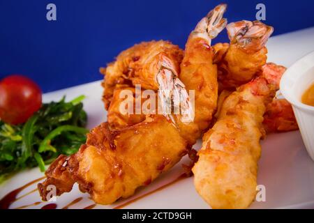 Gebratene Tigergarnelen im Teig serviert mit süßer und saurer Sauce, Nori-Algen und Kirschtomaten auf einem rechteckigen Teller. Stockfoto