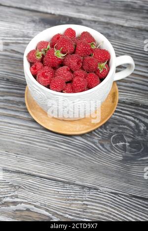 Himbeeren in einem großen weißen Becher. Auf Holzbrettern mit einer schönen Textur. Stockfoto