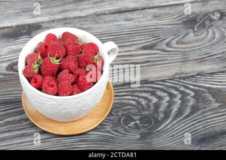 Himbeeren in einem großen weißen Becher. Auf Holzbrettern mit einer schönen Textur. Stockfoto