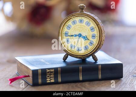 Alter Wecker auf der Heiligen bibel mit Blumen auf Holz Tabellenhintergrund Stockfoto
