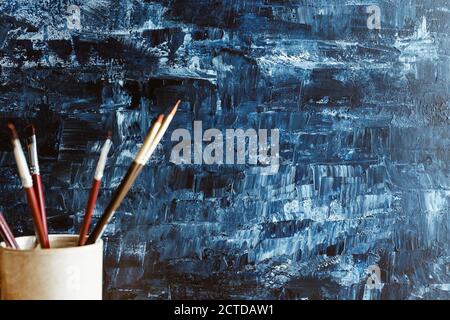 Verschwommene Malpinsel in einem Keramikbecher vor einem blauen abstrakten Hintergrund. Stockfoto