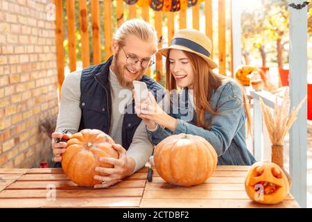 Halloween Vorbereitung Konzept. Junges Paar sitzt am Tisch auf der Veranda machen Jack-o'-Laterne Foto von Kürbis lächelnd glücklich Stockfoto
