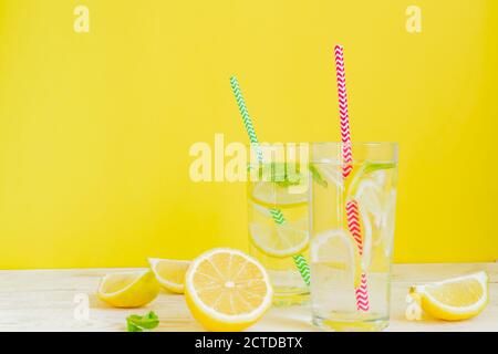 Zwei Gläser selbstgemachte Limonade mit Zitronen, Minze und Papierstroh auf gelbem Hintergrund. Erfrischendes Getränk im Sommer. Stockfoto
