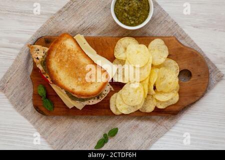 Hausgemachtes Pesto Chicken Sandwich mit Kartoffelchips auf rustikalem Holzbrett, Draufsicht. Flach, von oben, über Kopf. Stockfoto