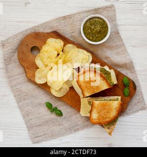 Hausgemachtes Pesto Chicken Sandwich mit Kartoffelchips auf einem rustikalen Holzbrett, Blick von oben. Flach liegend, von oben, Draufsicht. Stockfoto