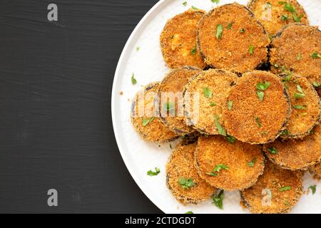 Hausgemachter Knoblauch Parmesan gebacken Aubergine auf einem Teller auf schwarzem Hintergrund, Overhead-Ansicht. Flach liegend, Draufsicht, von oben. Speicherplatz kopieren. Stockfoto