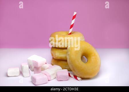 Vier Donuts oder Classic Donuts Stack mit Marshmallows und zwei Red Stripe Stroh auf einem weißen und rosa Hintergrund. Stockfoto