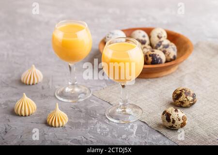 Süßer Eierlikör im Glas mit Wachteleiern und Baisenkraut auf grauem Betongrund. Seitenansicht, Nahaufnahme. Stockfoto
